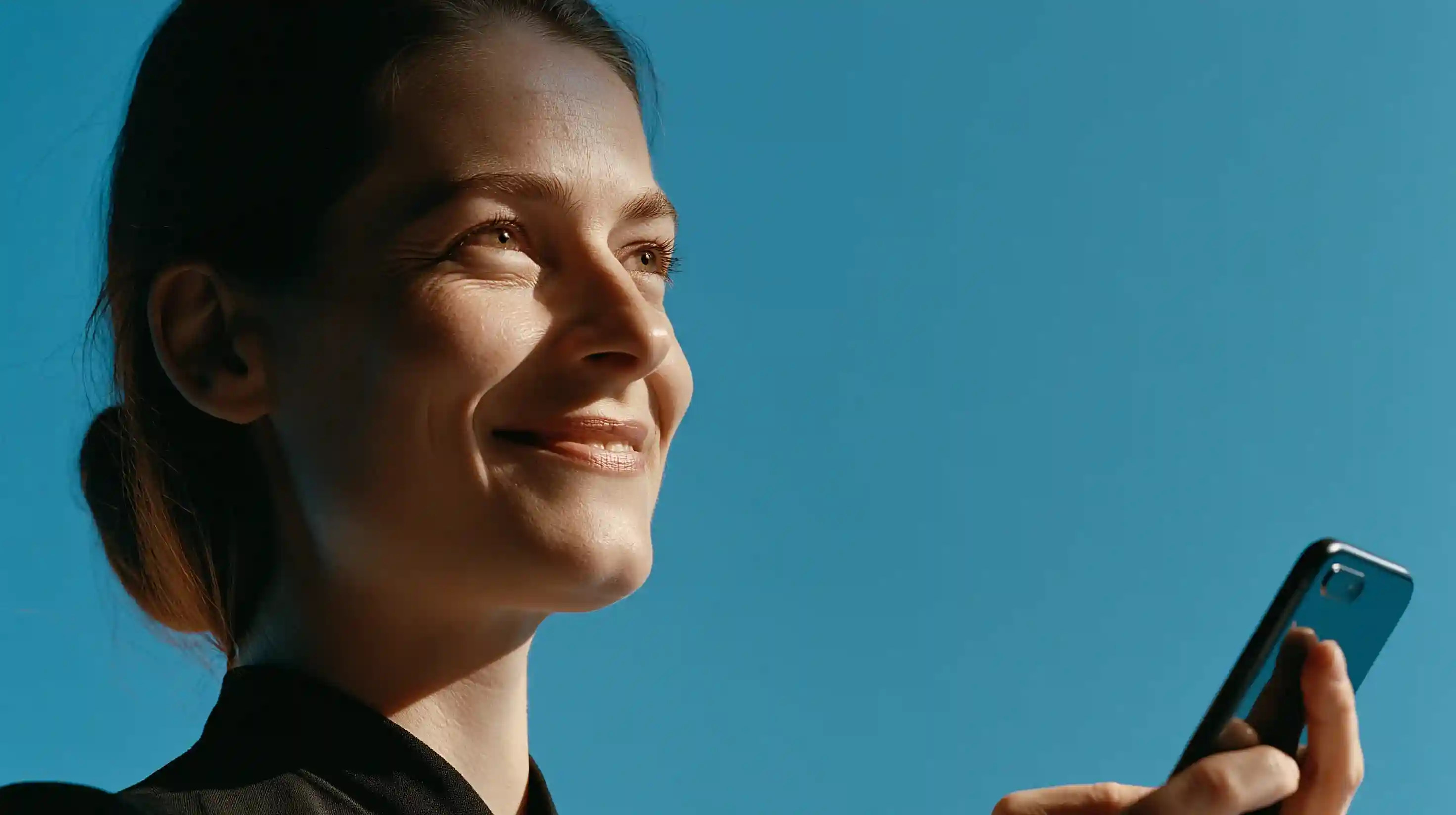 Smiling woman holding a smartphone outdoors against a blue sky